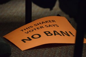 A sign sits at the feet of a community member. The neon orange, pink, yellow and green signs were handed out by Clint Evans before the meeting.