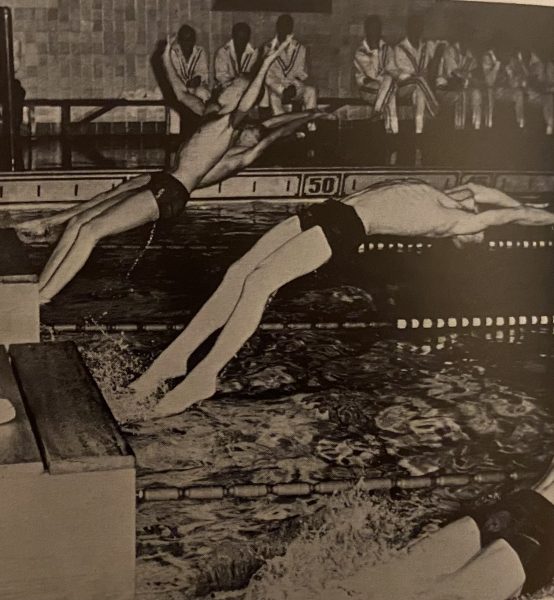 Swimmers launch from the starting blocks for a backstroke heat during a 1957 swim meet held at the high schools pool.