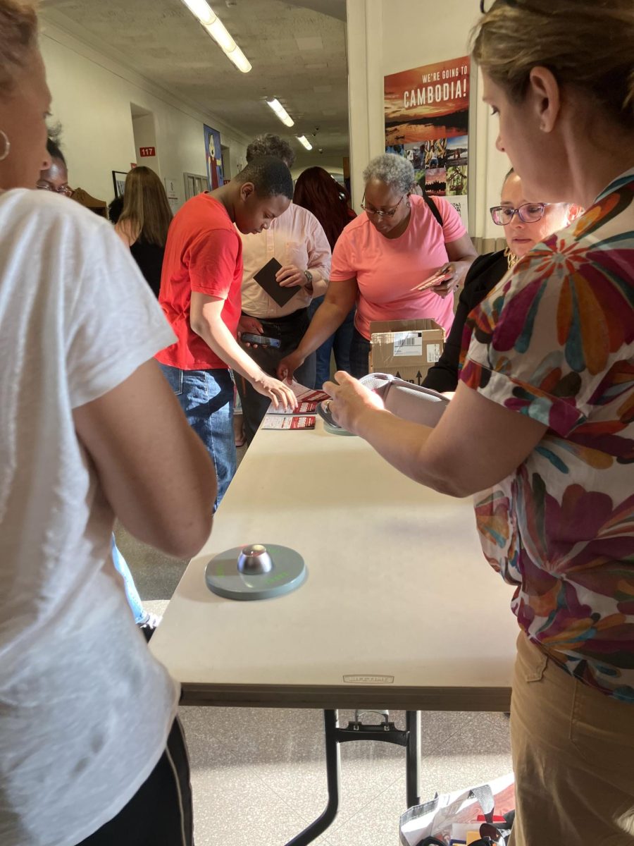 Assistant Principal Lisa Demkowicz staffs a table where parents who attended a meeting about the new electronic device policy examine Yondr pouches and unlocking mechanisms at the high school Aug. 13.