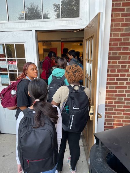 Students line up outside the lower cafeteria doors and await their turn for bag checks and metal detection before school Sept. 19. Recently, rainy, cold weather has prevented frequent random checks, which will continue until the district pilots a walk-through system in December.