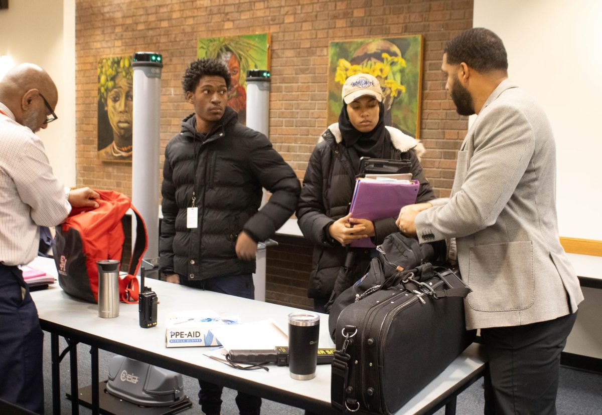 Sophomore Isahq Shaheed and junior Maysun Abdush-Shaheed wait while Director of Security Vic Ferrell and Interim Principal Isaiah Wyatt check their backpacks in the egress Jan. 23. Students whose backpacks triggered the system underwent secondary screenings. 