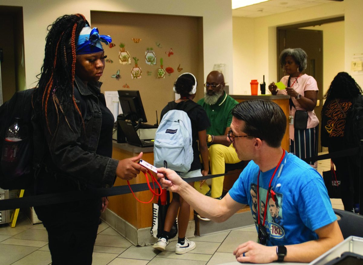 Assistant Principal Logan Cawley hands an ID to sophomore Jasyme Allen in the cafeteria during arrival Sept. 18.
