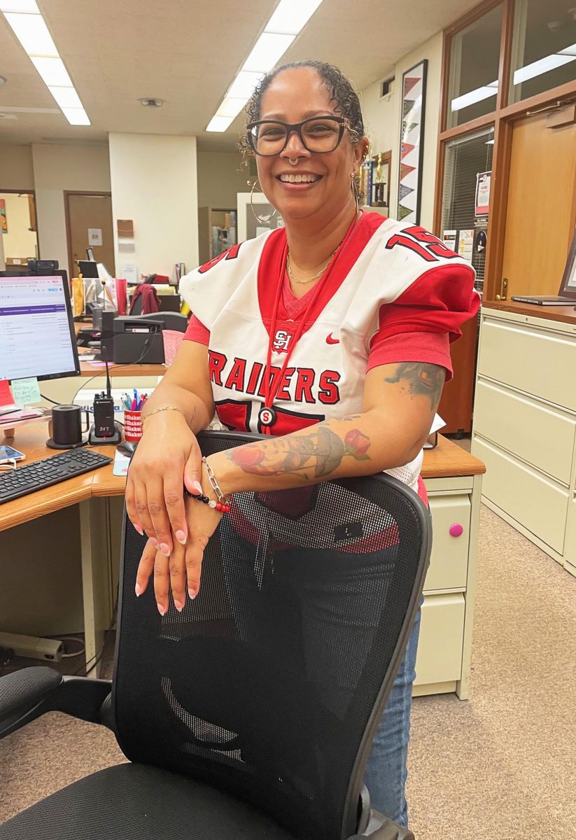 Administrative assistant Brooke Wright wears the jersey of senior Kingston Seals in the main office Oct. 3. Wright and the other staff chosen by senior players to wear jerseys today will be honored at tonight's Faculty/Staff Teacher Appreciation football game. 