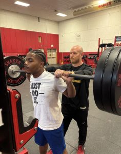 Head strength and conditioning coach Joseph Schlesinger spots junior Angelo McCoy as he prepares to back squat after school in the Raider Athletic Center May 8.
