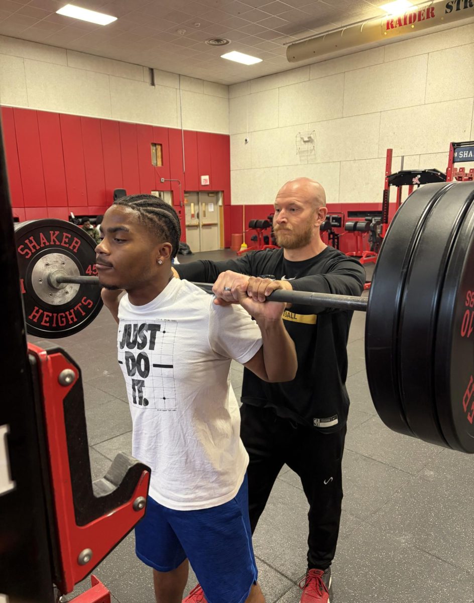 Head strength and conditioning coach Joseph Schlesinger spots junior Angelo McCoy as he prepares to back squat after school in the Raider Athletic Center May 8.
